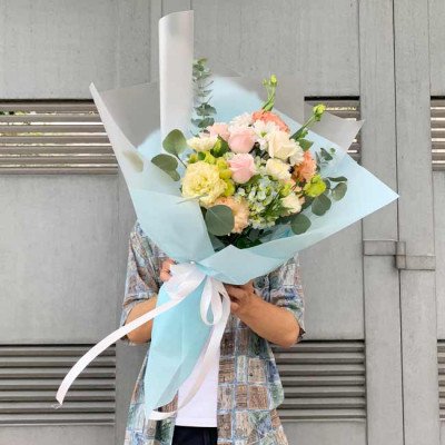Bouquet with pink, yellow, white, and green flowers, wrapped in light blue paper with a white ribbon.