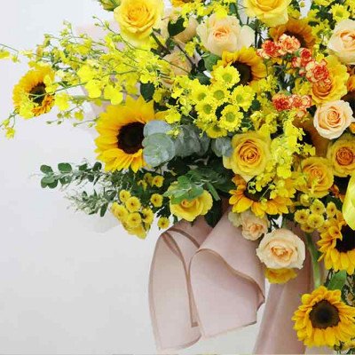 A large bouquet of yellow flowers, including sunflowers, roses, and orchids, with a pink ribbon.