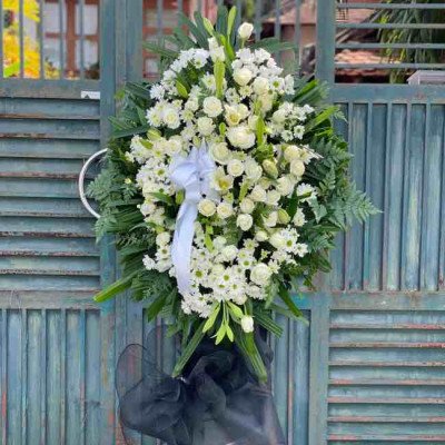White funeral wreath with lilies, chrysanthemums, roses, and astilbe on a wooden gate.