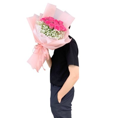 Man holding a bouquet of pink roses and baby's breath wrapped in pink paper.