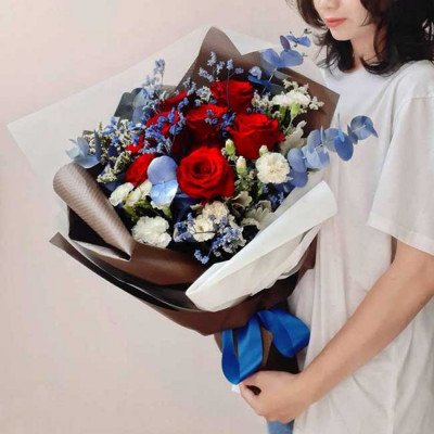 A bouquet of red roses with blue and white accent flowers and eucalyptus leaves, tied with a blue ribbon.