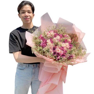 Man in black t-shirt and jeans holding a large bouquet of pink and purple roses.