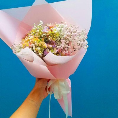 A hand holding a pink-wrapped bouquet of hydrangeas and baby's breath.