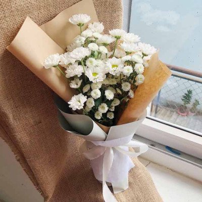 Bouquet of white chrysanthemums and calimero flowers wrapped in paper with a white ribbon.