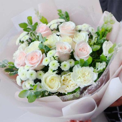 Bouquet of pink and white roses, carnations, and small white flowers in pink paper.