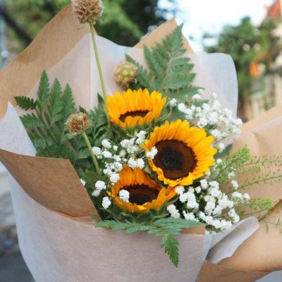 A bouquet of sunflowers, baby's breath, and greenery wrapped in brown paper.