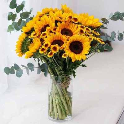 A vase overflowing with sunflowers and smaller yellow flowers, accented with eucalyptus leaves.