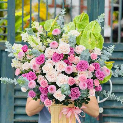 Floral arrangement in a wooden box with pink and white roses, green anthurium, and other flowers.