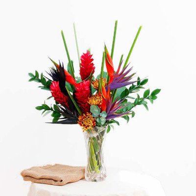 Tropical flower arrangement with red ginger, bird of paradise, and chrysanthemums in a glass vase.