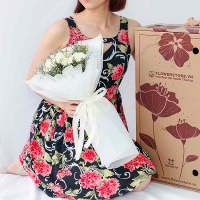 Woman in a floral dress holding a white bouquet next to a flower delivery box.