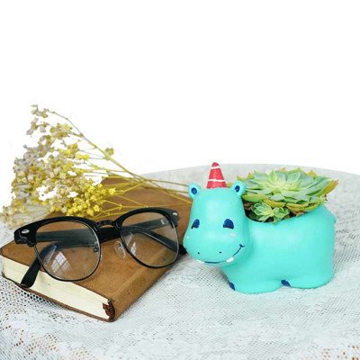 Cute green hippo planter with a succulent, sitting next to glasses and dried flowers.