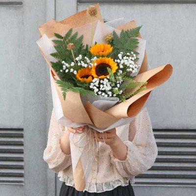Bouquet of sunflowers, baby's breath, and greenery wrapped in brown and white paper.