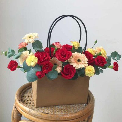 Brown floral gift bag with red roses, gerbera daisies, and carnations.