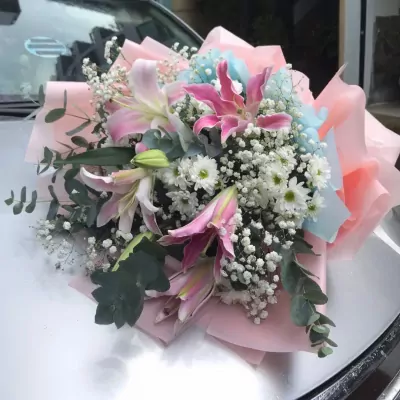 Pink and white lilies with baby's breath and greenery, wrapped in pink and blue paper.