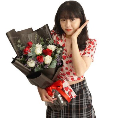 Young woman with a bouquet of red and white roses, eucalyptus, and purple flowers, wrapped in black paper with a red ribbon.