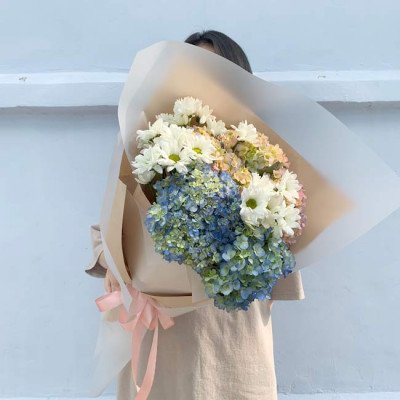 Bouquet of blue hydrangeas and white daisies wrapped in paper.