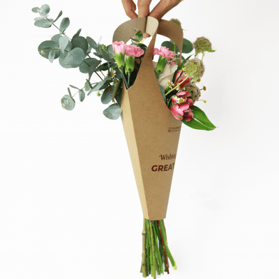 A hand holds a bouquet of flowers in a brown paper cone holder with "Wishes GREAT" printed on it.
