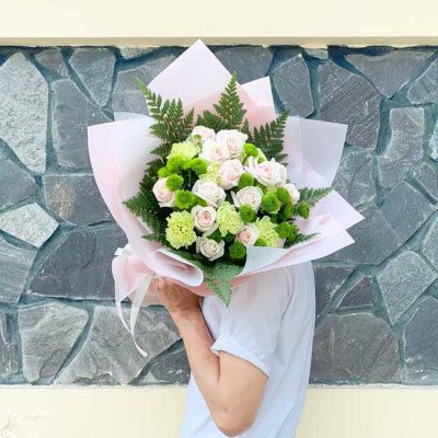 Bouquet of pink roses and green chrysanthemums wrapped in pink paper.