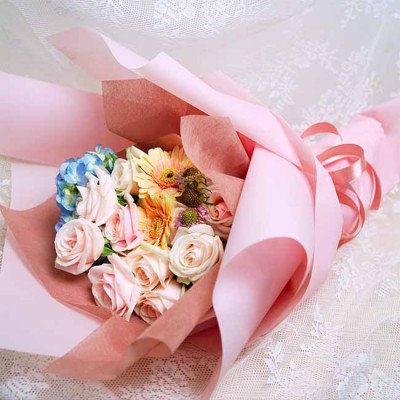 Pink and peach roses with blue hydrangea, gerbera daisies, and other flowers wrapped in pink paper.