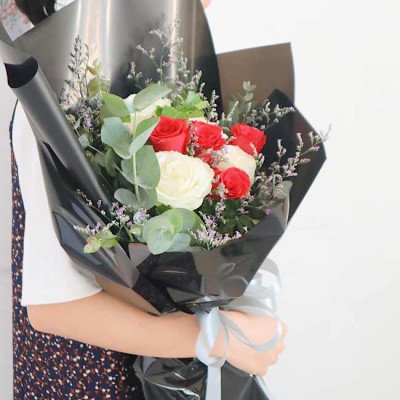 Bouquet of red and white roses with eucalyptus and baby's breath, wrapped in black paper.