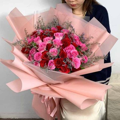 Buket mawar merah dan pink yang dibungkus kertas krep merah muda.
