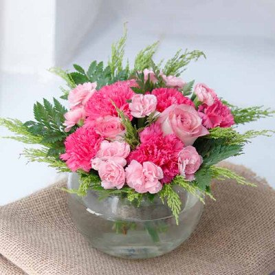 A pink carnation and rose floral arrangement in a clear glass bowl.