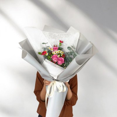 Pink roses, baby's breath, and eucalyptus in a bouquet wrapped in white and grey paper.