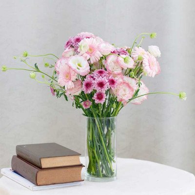Pink and purple flowers in a glass vase with books on a table.
