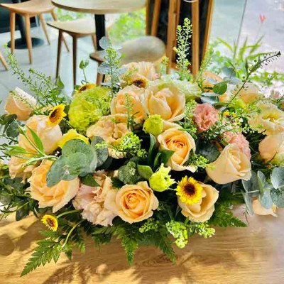 Bouquet of peach and yellow roses, sunflowers, and greenery on a wooden table.