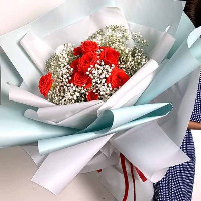 Bouquet of red roses and baby's breath flowers wrapped in white and light blue paper.