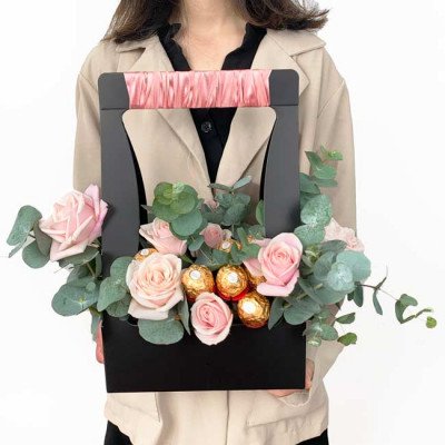 Pink roses and Ferrero Rocher chocolates in a black gift box with pink ribbon handle.