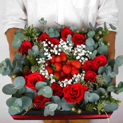 Red roses, strawberries, and baby's breath arranged in a dark box with eucalyptus.