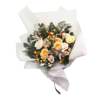 Bouquet of yellow, peach, and cream roses with greenery, wrapped in white paper.
