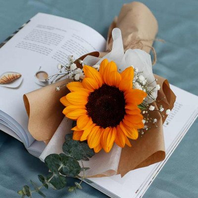 A sunflower bouquet rests on an open book next to a croissant and coffee.