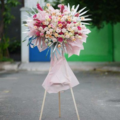 A tall flower arrangement with pink and orange roses, on a wooden easel.