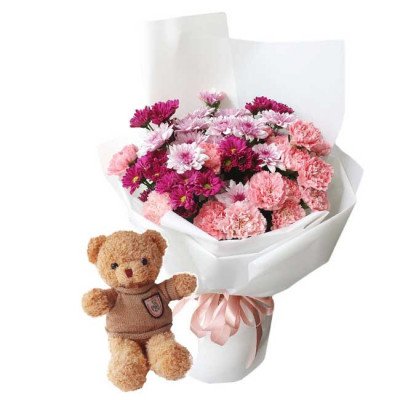A teddy bear and a bouquet of pink and purple flowers in white wrapping, tied with a pink ribbon.