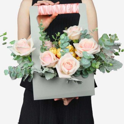 Pink roses and Ferrero Rocher chocolates in a grey gift box with a pink ribbon handle.