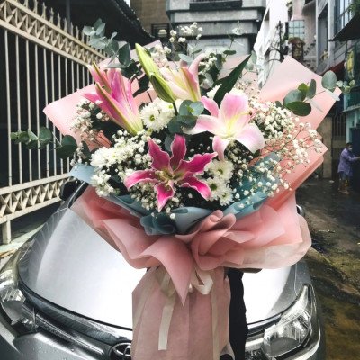 Pink and white lilies with baby's breath in pink and blue paper wrapping on a car hood.