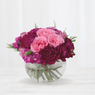 Pink roses and deep purple carnations in a clear glass bowl.