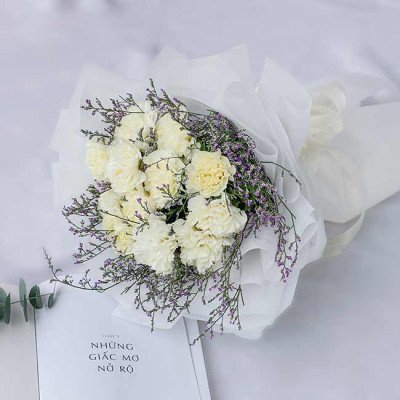 White carnation bouquet wrapped in white paper, with purple accent flowers.
