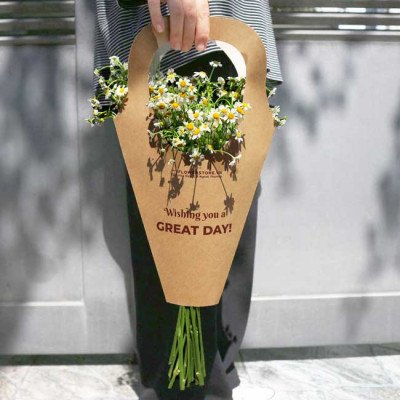Person holding brown paper cone with daisies and "Wishing you a GREAT DAY!"