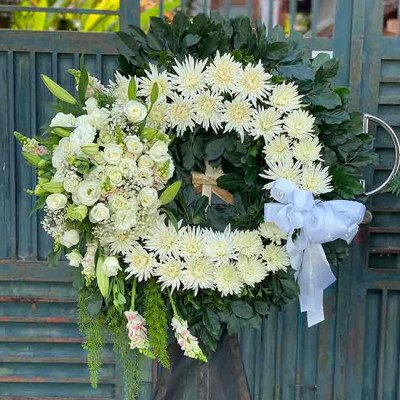 Funeral wreath with white roses, chrysanthemums, lilies, and greenery, adorned with a white ribbon.