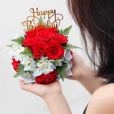 Birthday flower arrangement with red roses, red carnations, hydrangeas, and "Happy Birthday" topper.