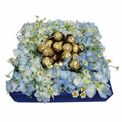 A blue floral arrangement with Ferrero Rocher chocolates and daisy accents in a dark blue box.