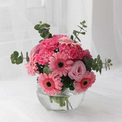 Pink gerbera daisies, carnations, and roses in a clear glass vase with eucalyptus.
