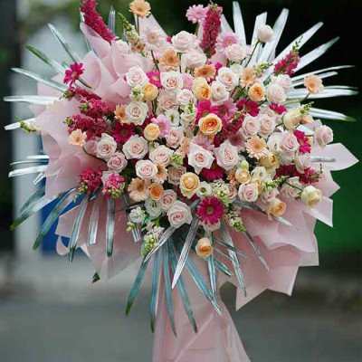 Floral arrangement in pink and orange tones with roses, daisies, and greenery.