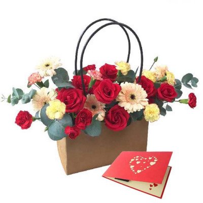 A floral arrangement in a brown bag with a red card and hearts.