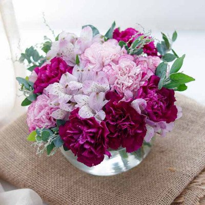 Bouquet of pink and purple carnations and alstroemeria in a glass vase on burlap.