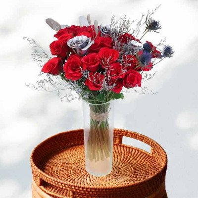 A vase of red and silver roses with dried flowers on a rattan tray.
