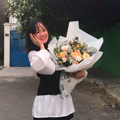 Woman holding a bouquet of orange and cream roses and carnations.